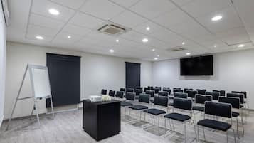 Ein Konferenzraum mit Projektor, Rednerpult, Reihen von Stühlen, einer Tafel und einer großen Leinwand.