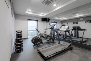 Une salle de sport équipée de tapis de course, de vélos elliptiques et de rangées de haltères.