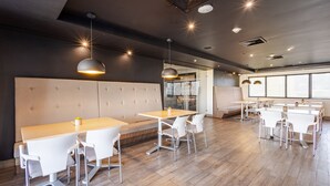 A modern dining area with wooden tables and white chairs, a cushioned bench, and pendant lighting.