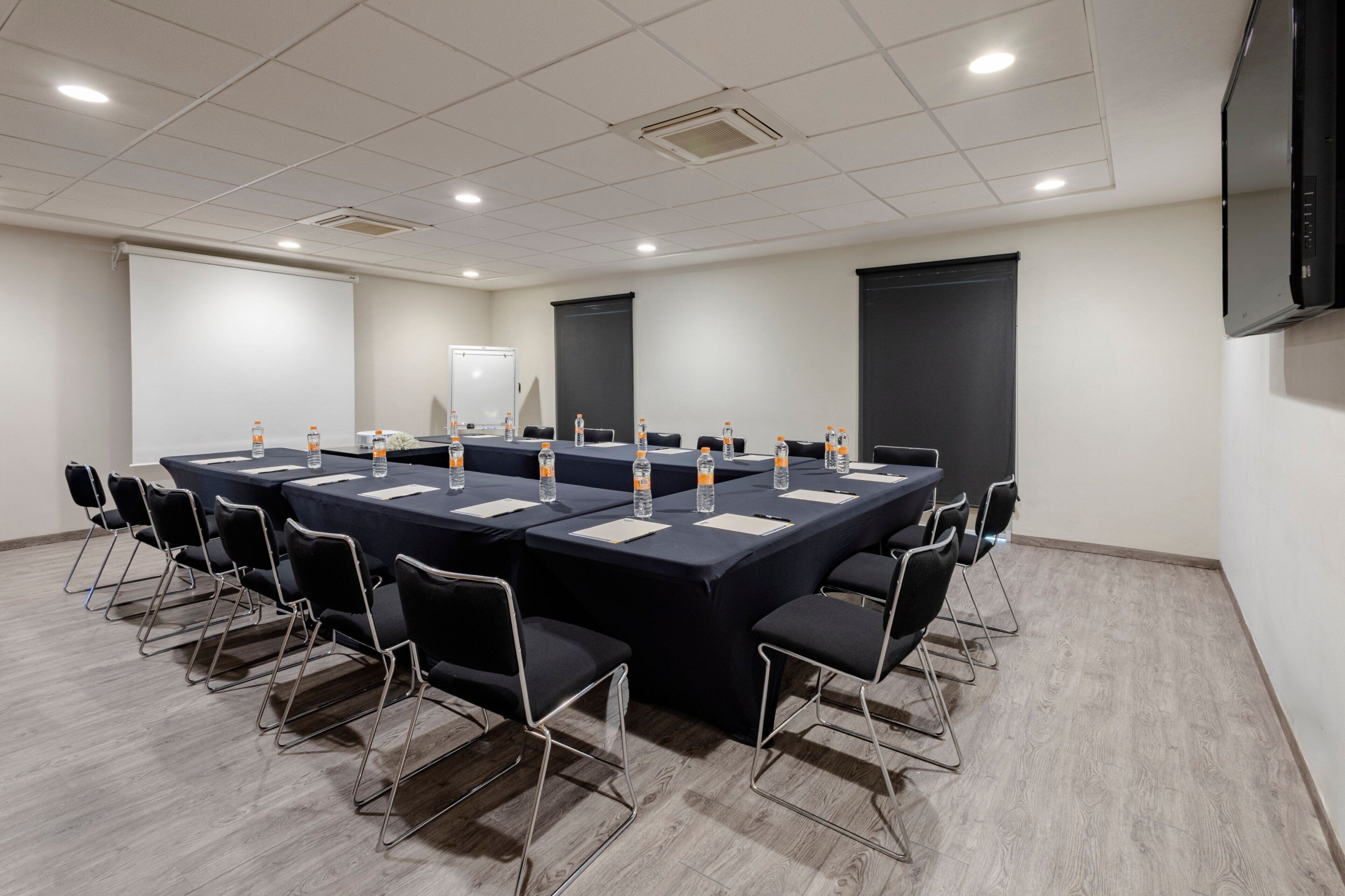 A conference room with a long table, chairs, water bottles, and a projector screen.