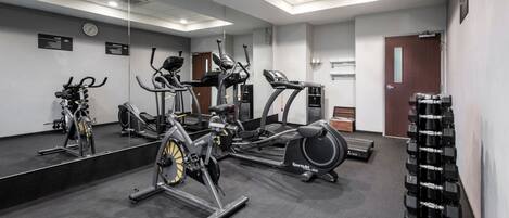 A gym with cardio machines, free weights, and a mirror.
