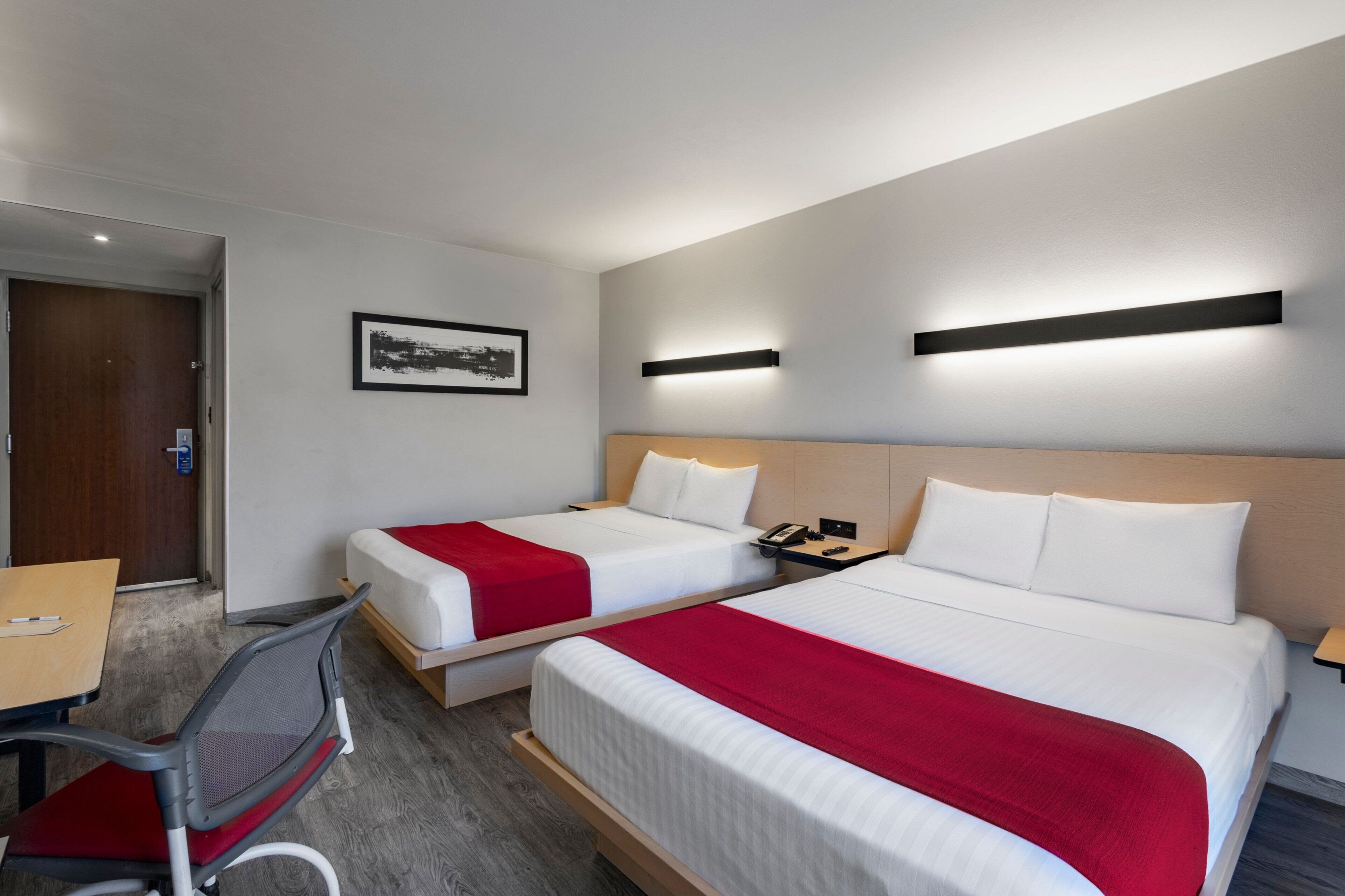 Habitación de hotel con dos camas, un escritorio, una silla y un cuadro en la pared.