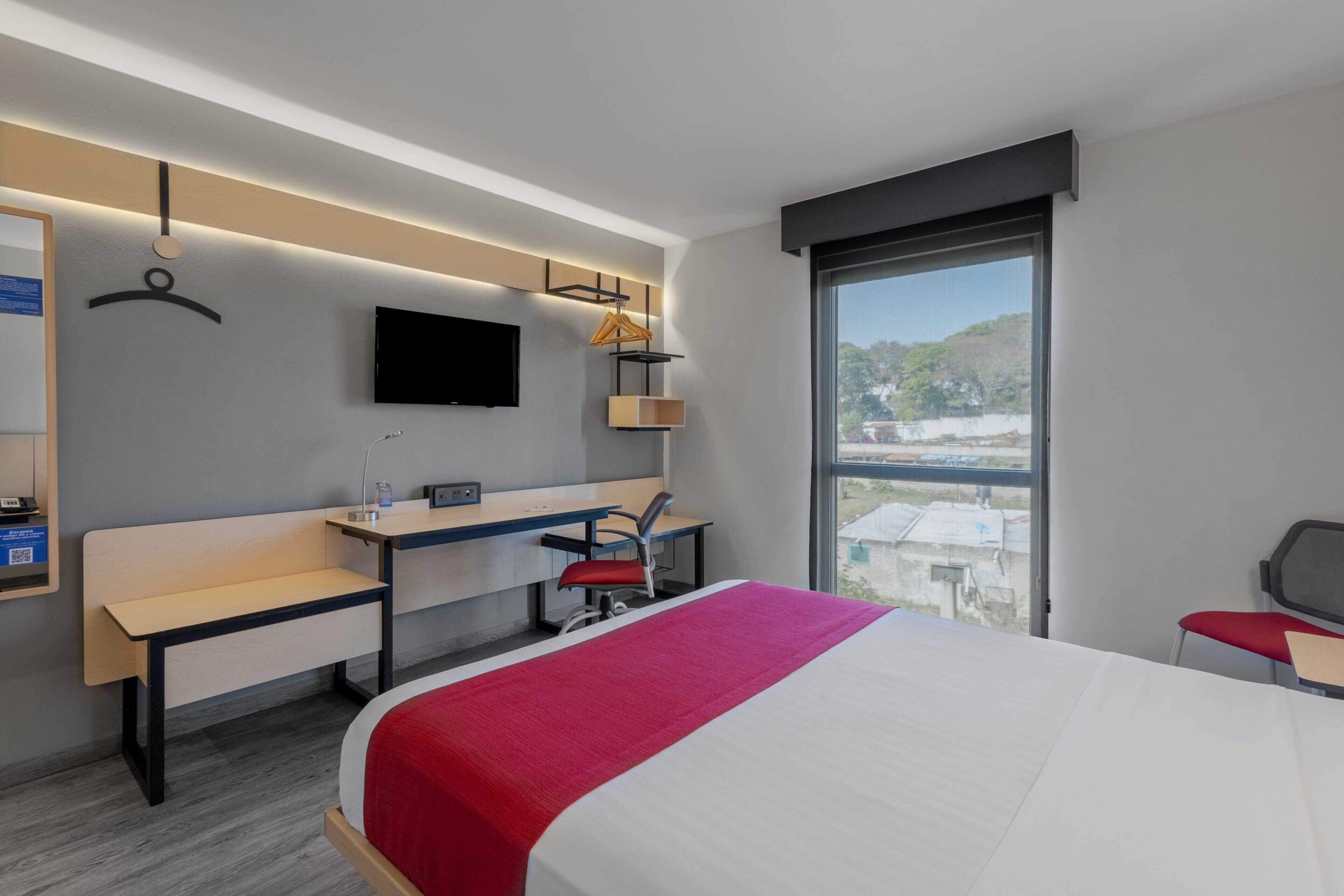 Ein modernes Hotelzimmer mit Bett, Schreibtisch, Stuhl und einem an der Wand befestigten Fernseher.