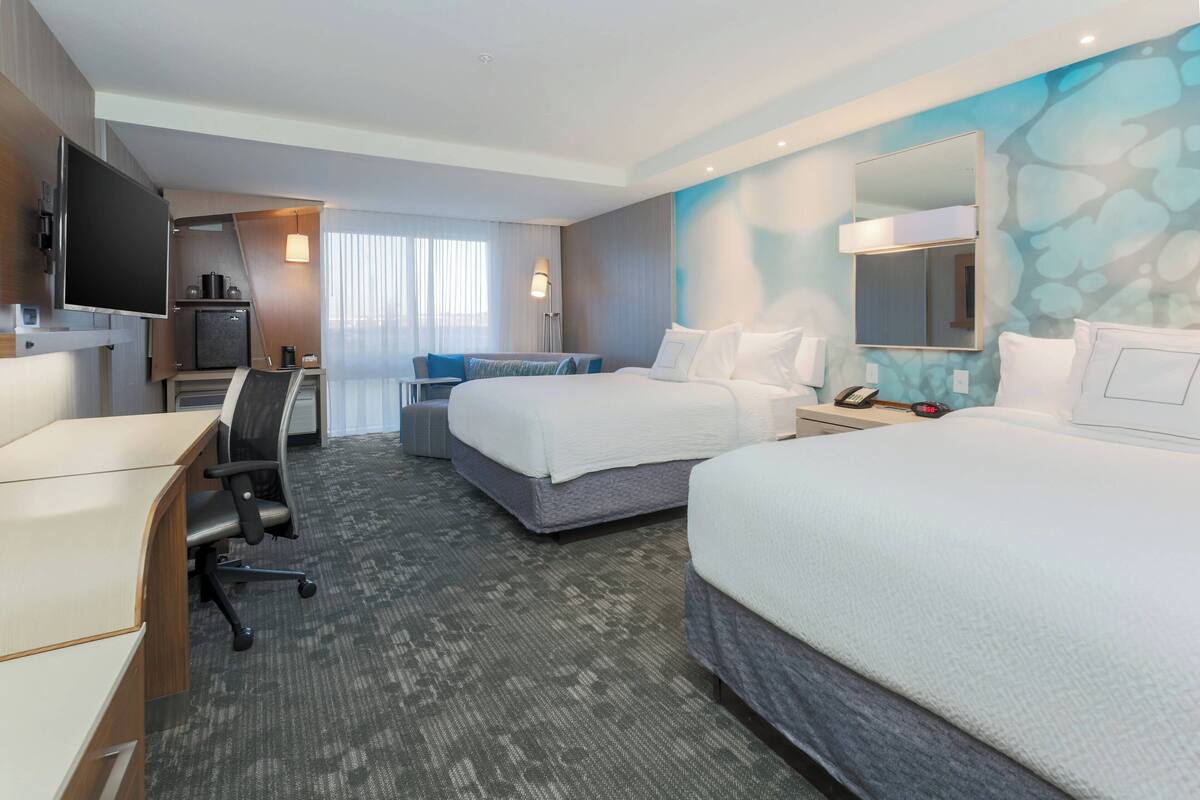 Ein Hotelzimmer mit zwei Betten, einem Schreibtisch, einem Fernseher, einer Minibar und einem Badezimmer.