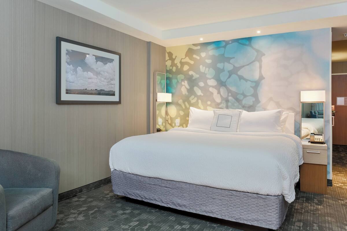Ein Hotelzimmer mit einem großen Bett, einem Sessel, einem Wandbild und einer dekorativen Wandmalerei.