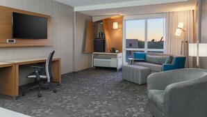 Een hotelkamer met een flatscreen televisie, een bureau, een comfortabele zithoek en een kleine kitchenette.