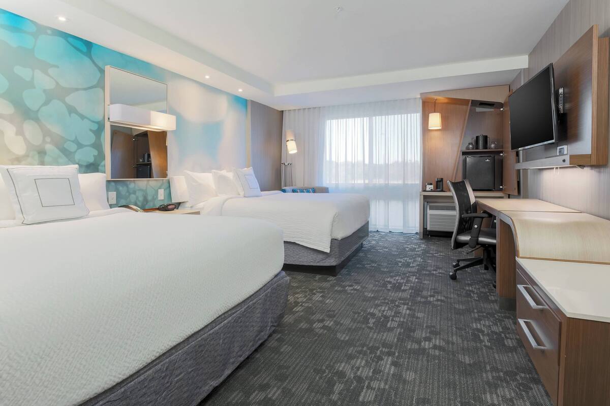 Ein Hotelzimmer mit zwei Betten, einem Schreibtisch, einem Fernseher und einer Minibar.