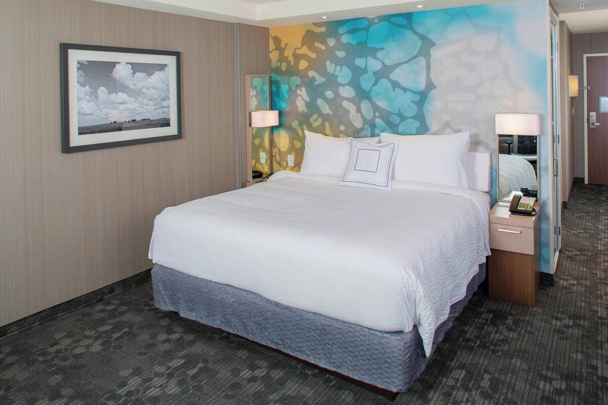 Ein Hotelzimmer mit einem großen Bett, zwei Nachttischen, einer Wandlampe und einem gerahmten Bild an der Wand.
