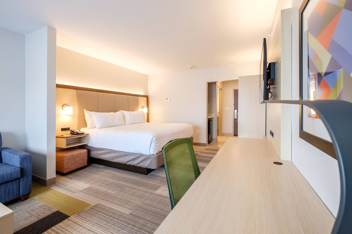 A hotel room with a bed, a desk, a chair, a TV, and a lamp.