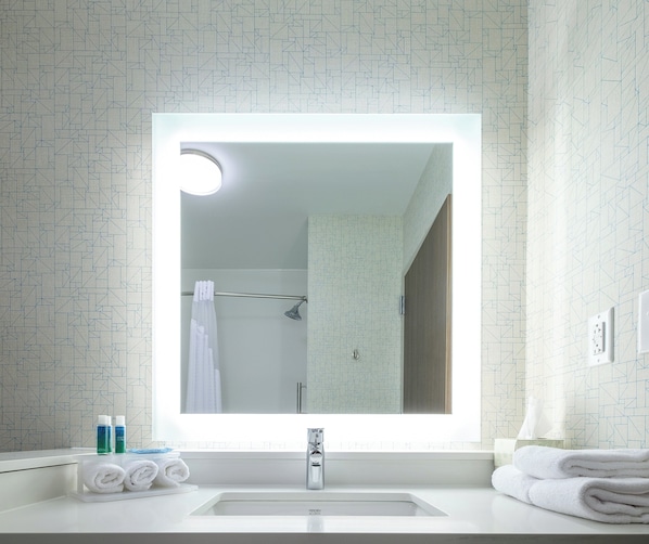 A bathroom with a modern sink, a mirror with a light, and a shower area.