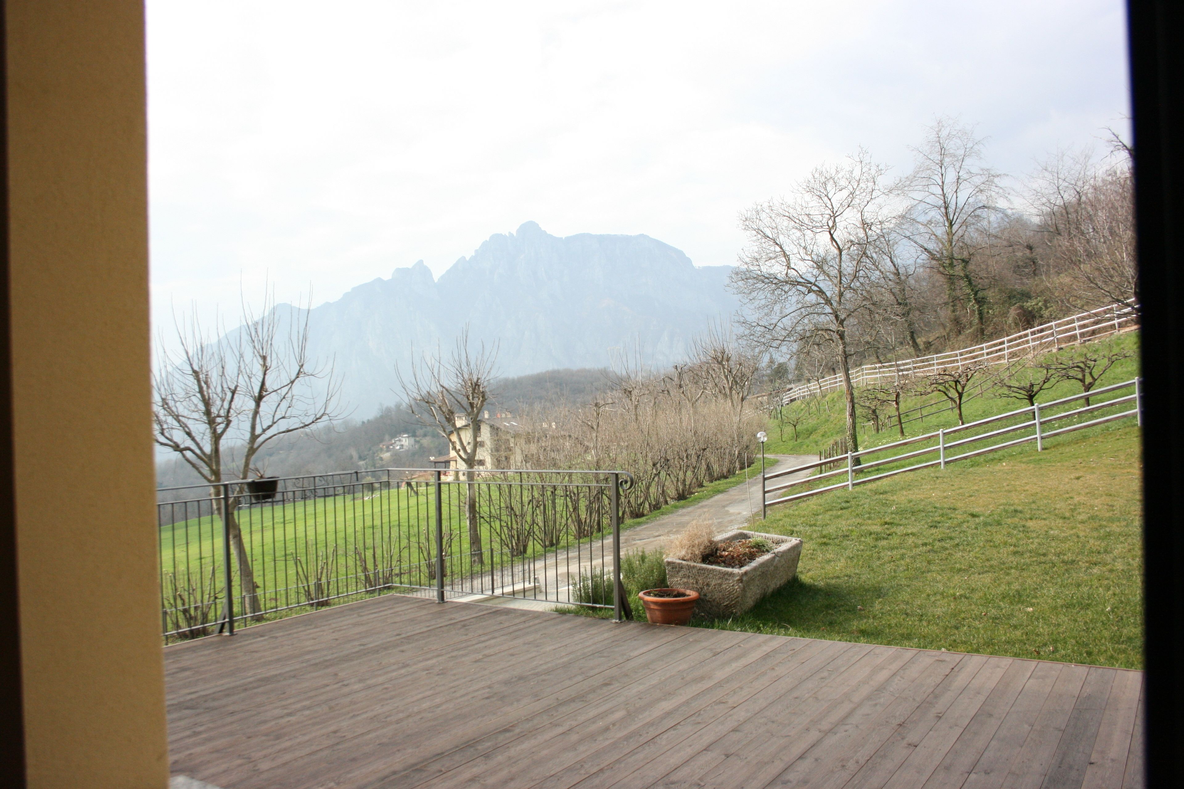 Una terraza de madera con vistas a un espacio verde y montañas al fondo.