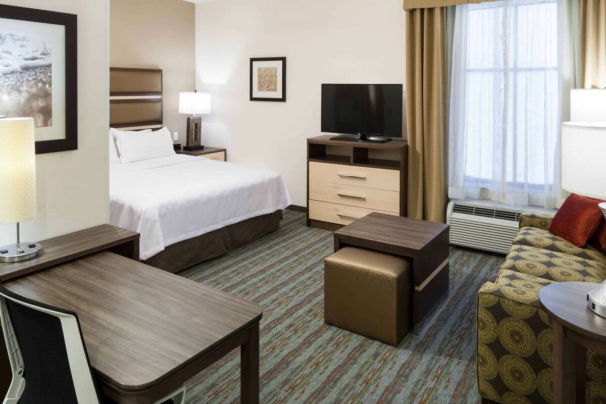 A hotel room with a bed, desk, TV, and a sofa.