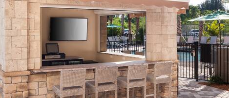 An outdoor bar area with stone walls, a flat-screen TV, and wicker bar stools.