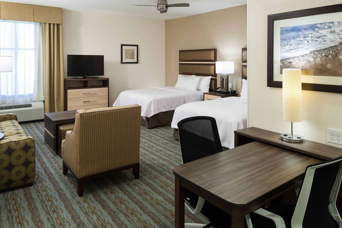A hotel room with two beds, a desk, a chair, a TV, and a window with curtains.
