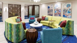 A modern lounge area with a yellow sofa, blue armchairs, and a round coffee table. - Homewood Suites by Hilton Cape Canaveral-Cocoa Beach (Cape Canaveral)