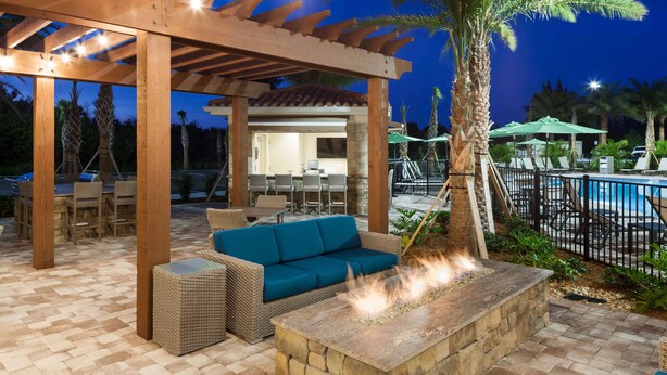 An outdoor patio area with a fire feature, wicker furniture, and a poolside setting. - Homewood Suites by Hilton Cape Canaveral-Cocoa Beach (Cape Canaveral)