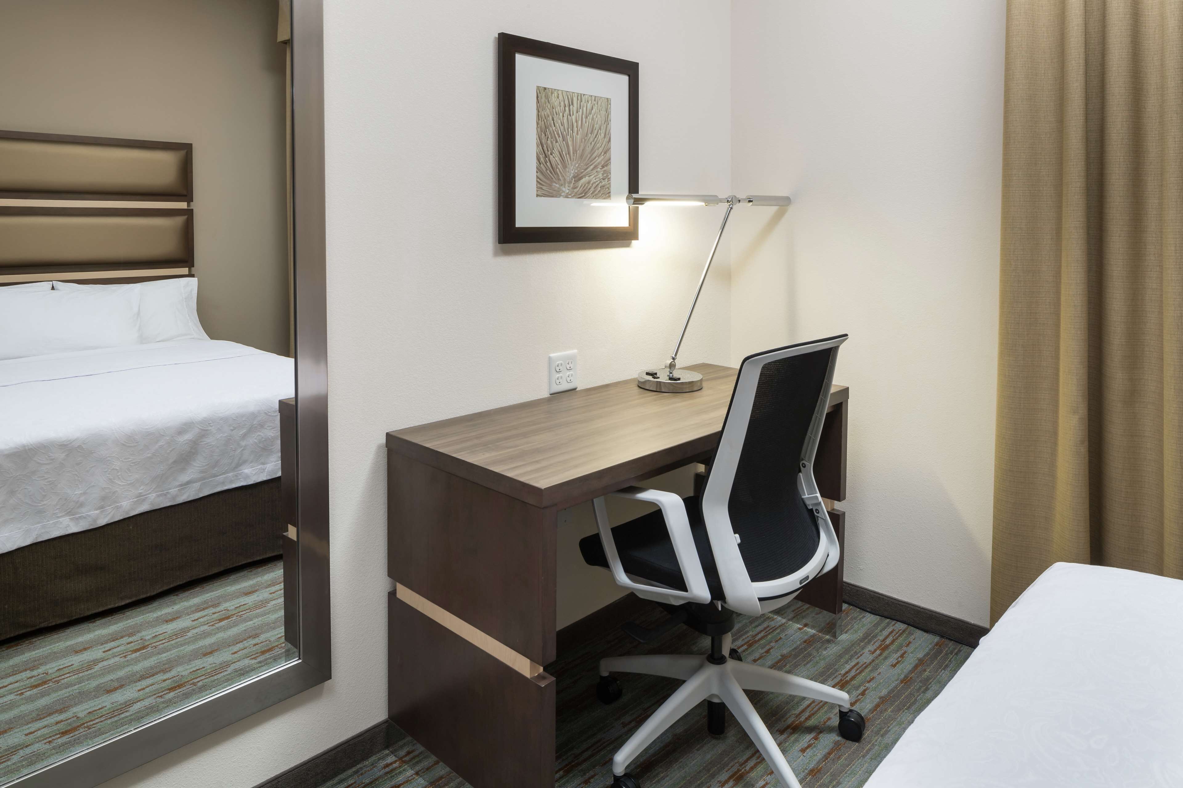 Une chambre d’hôtel avec un lit, un bureau et une chaise, un tableau encadré au mur et une lampe.