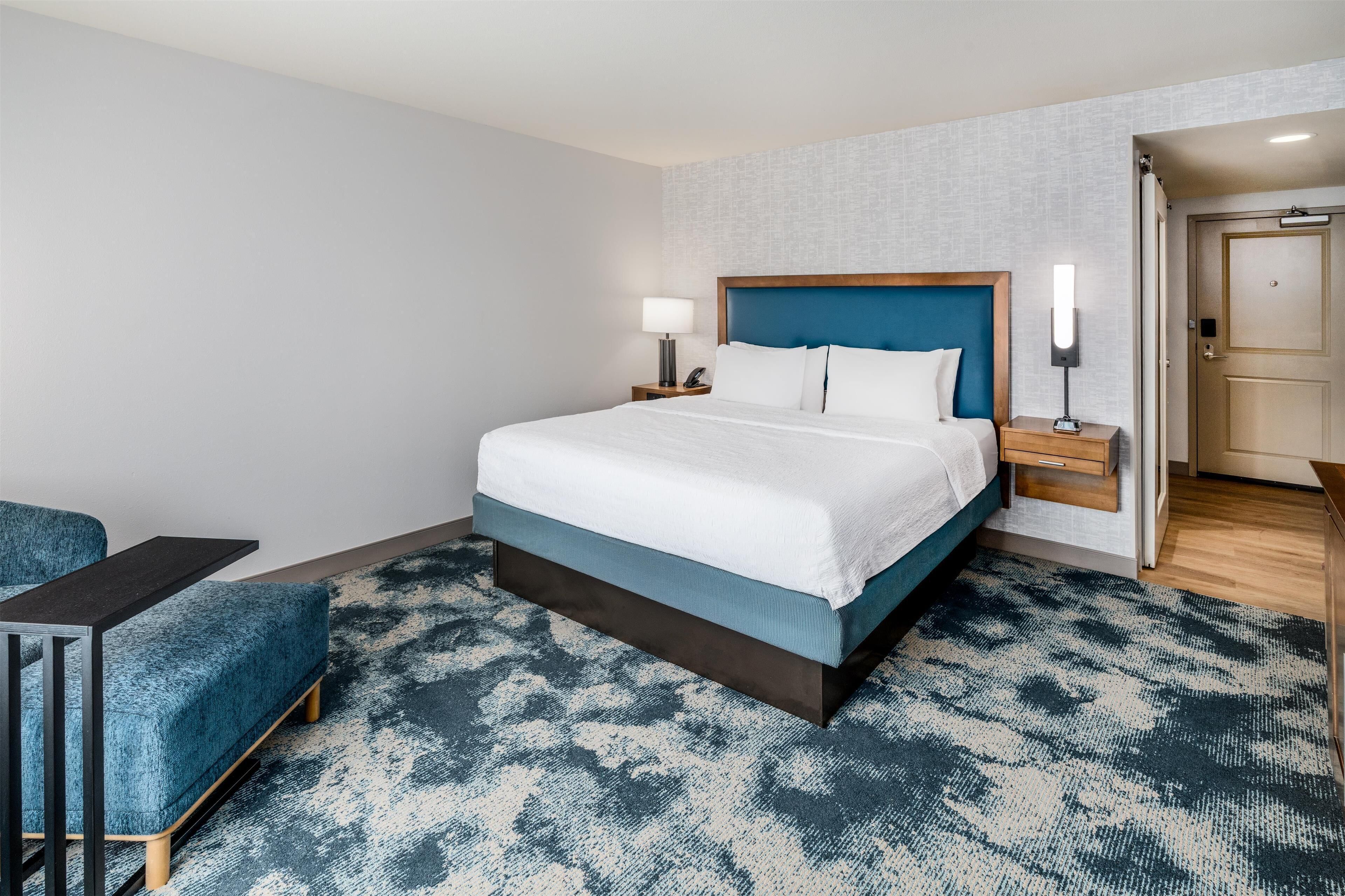 Habitación de hotel con una cama grande, mesitas de noche con lámparas, un escritorio y una alfombra estampada.