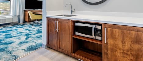 A modern hotel room with a wooden cabinet, a built-in microwave, a sink, and a large mirror.