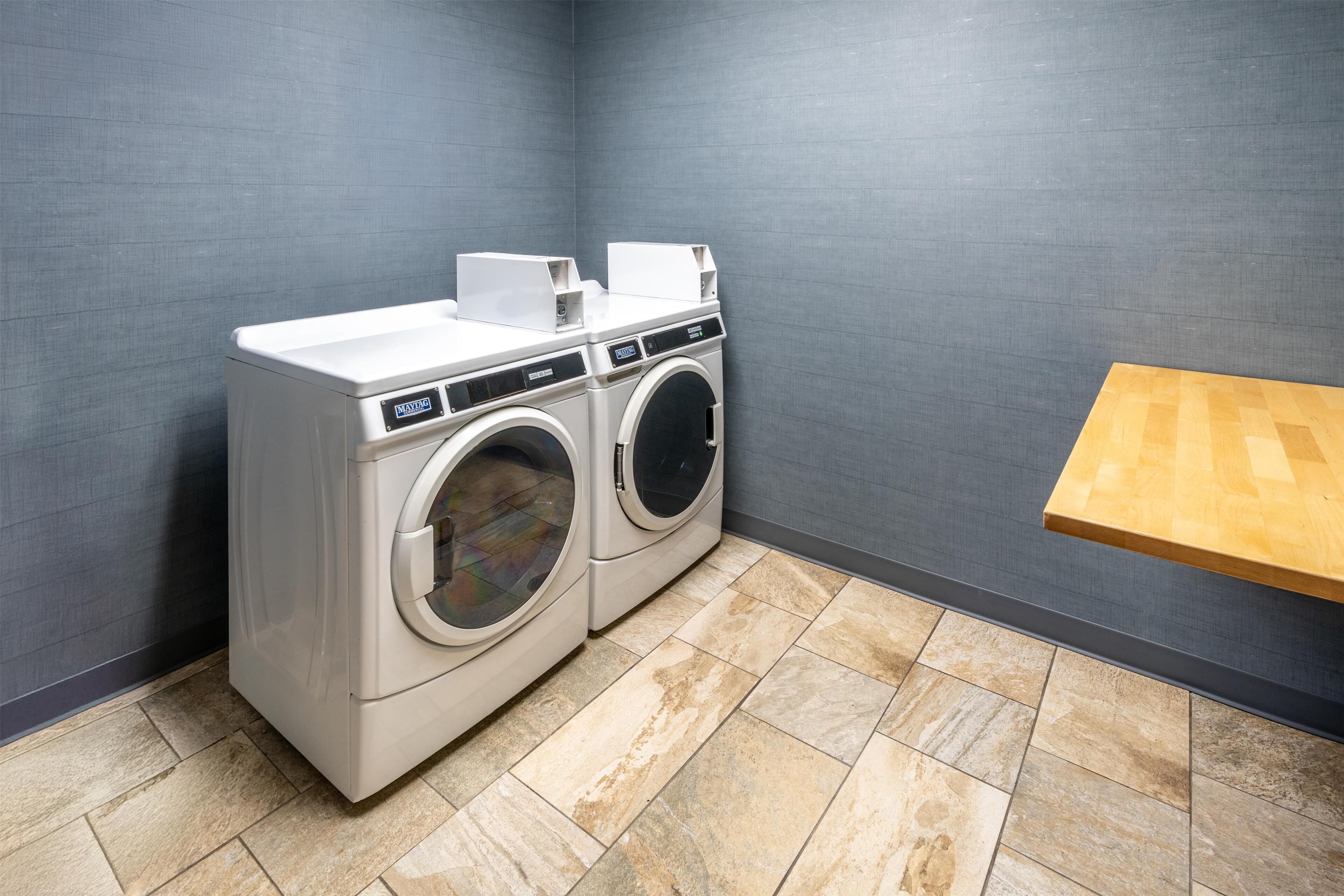 A laundry room with two front-loading washing machines, a wooden bench, and a grey textured wall.