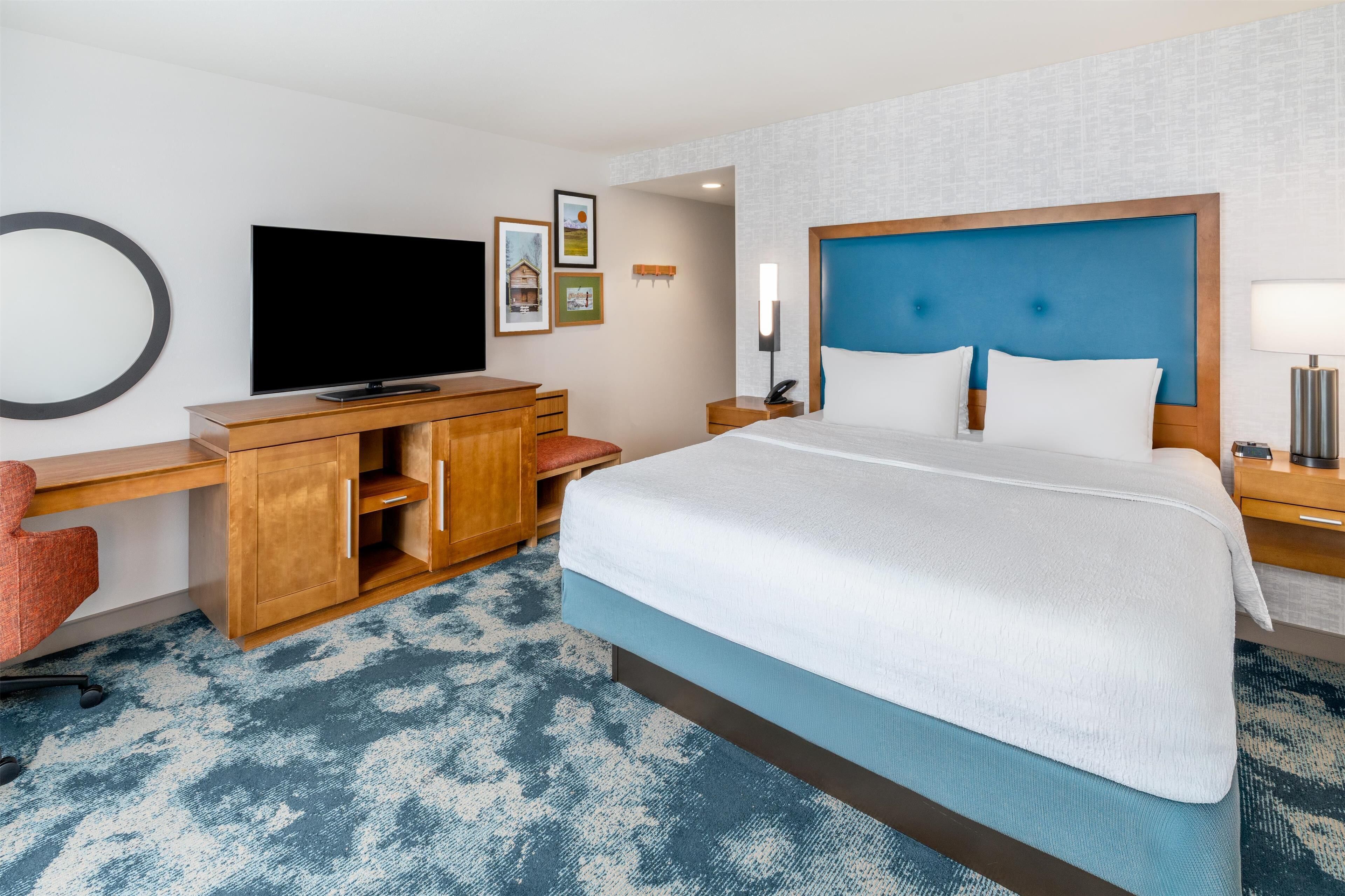 Ein Hotelzimmer mit einem großen Bett, einem Schreibtisch mit Fernseher, einem Sessel und einem kleinen Tisch.