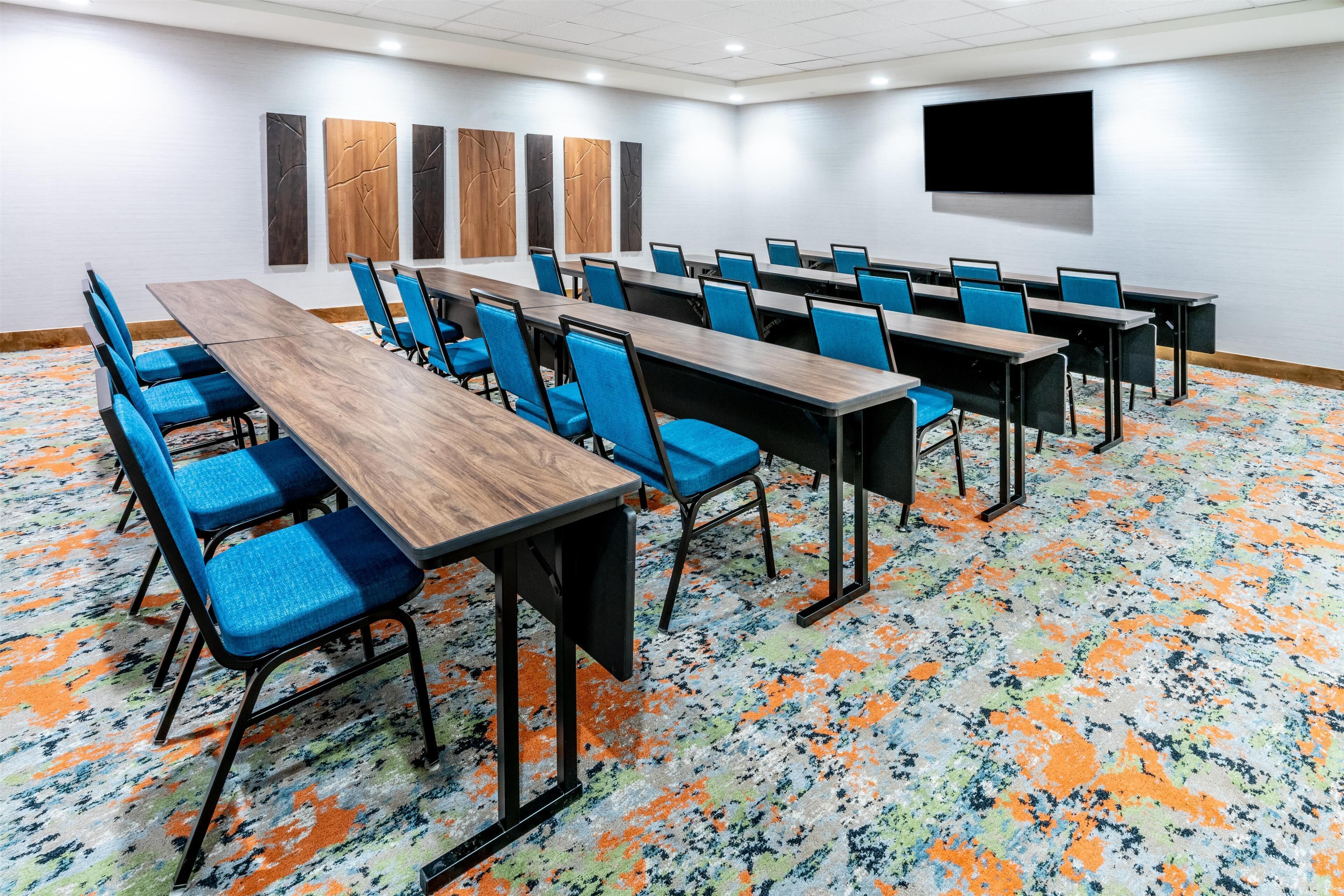 A conference room with multiple tables and chairs, a flat-screen TV mounted on the wall, and abstract wall art.