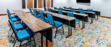 A conference room with multiple tables and chairs, a flat-screen TV mounted on the wall, and abstract wall art.