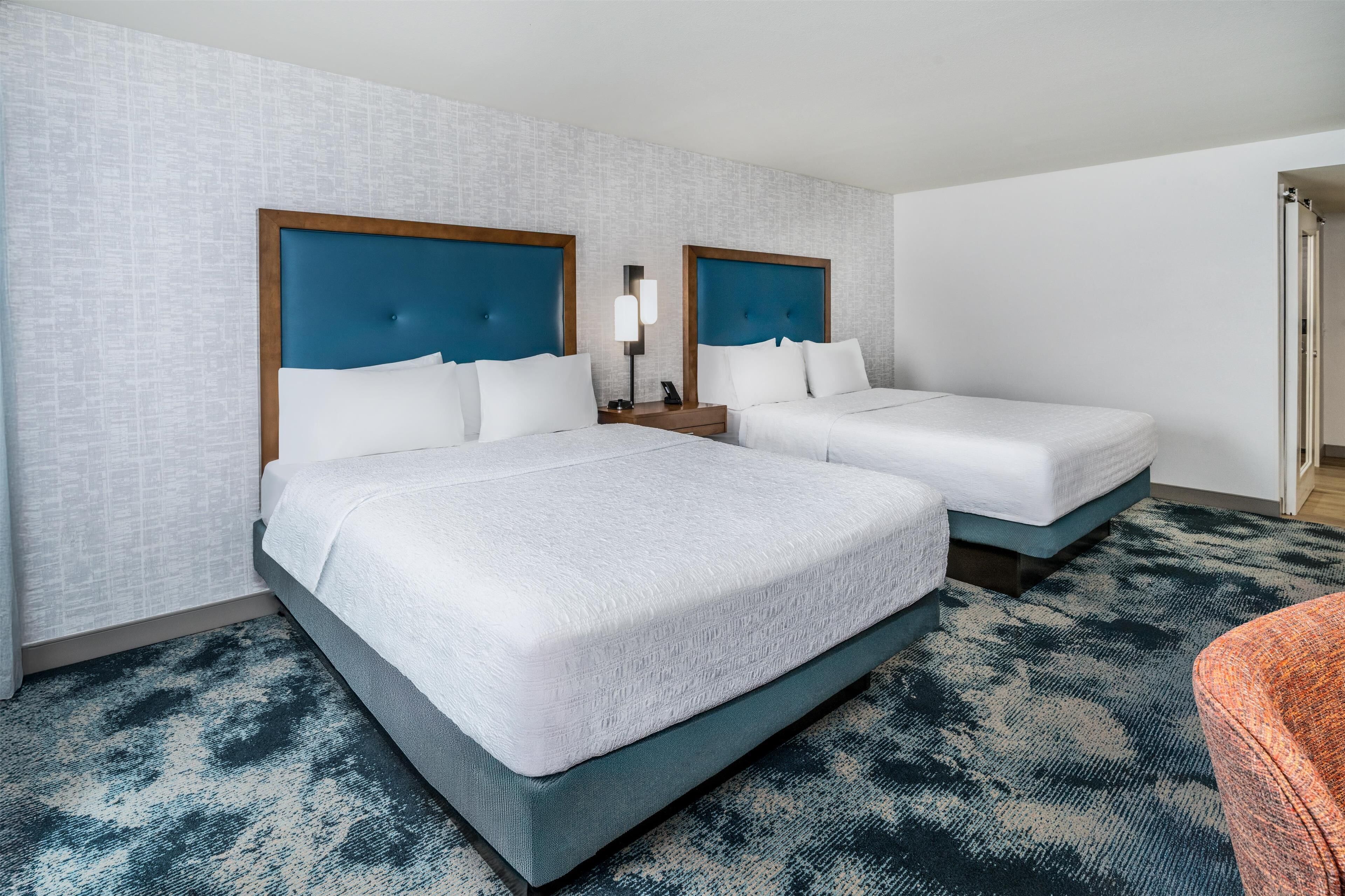 A hotel room with two beds, a nightstand, and a bathroom door.