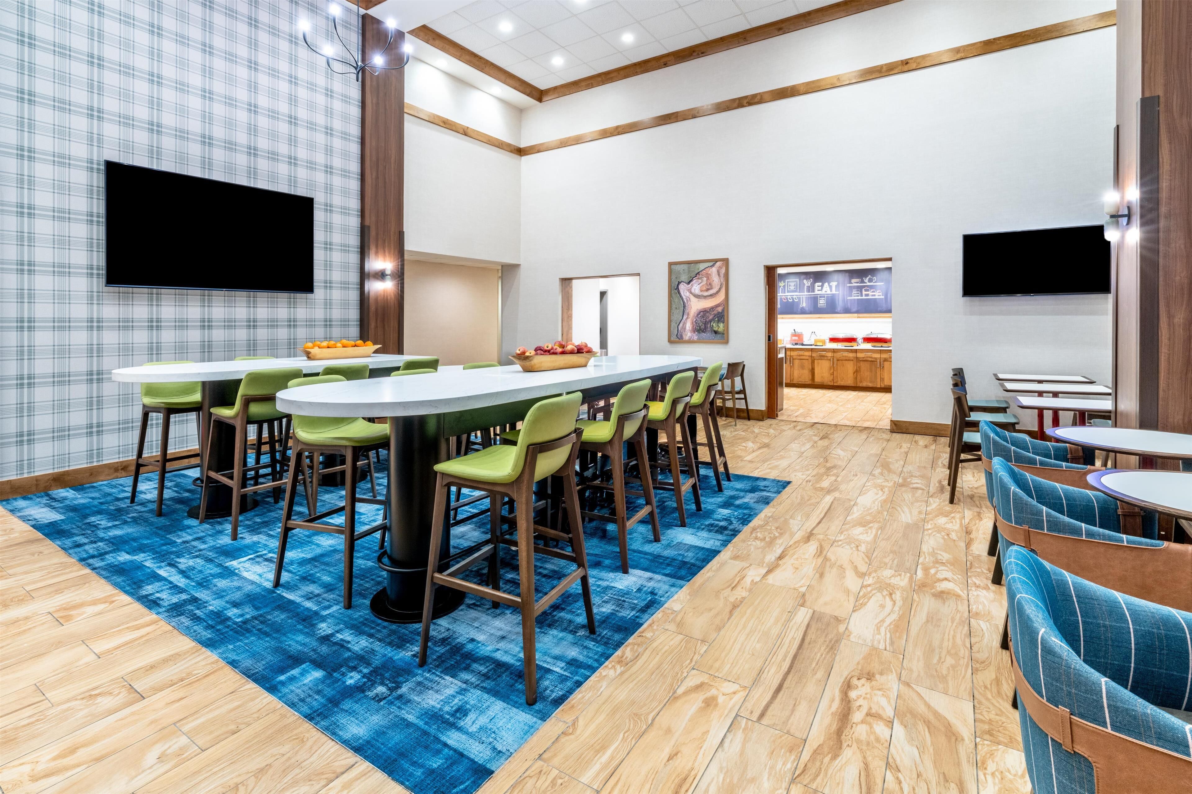 Un comedor moderno con una mesa larga, sillas verdes y un tapete azul estampado.