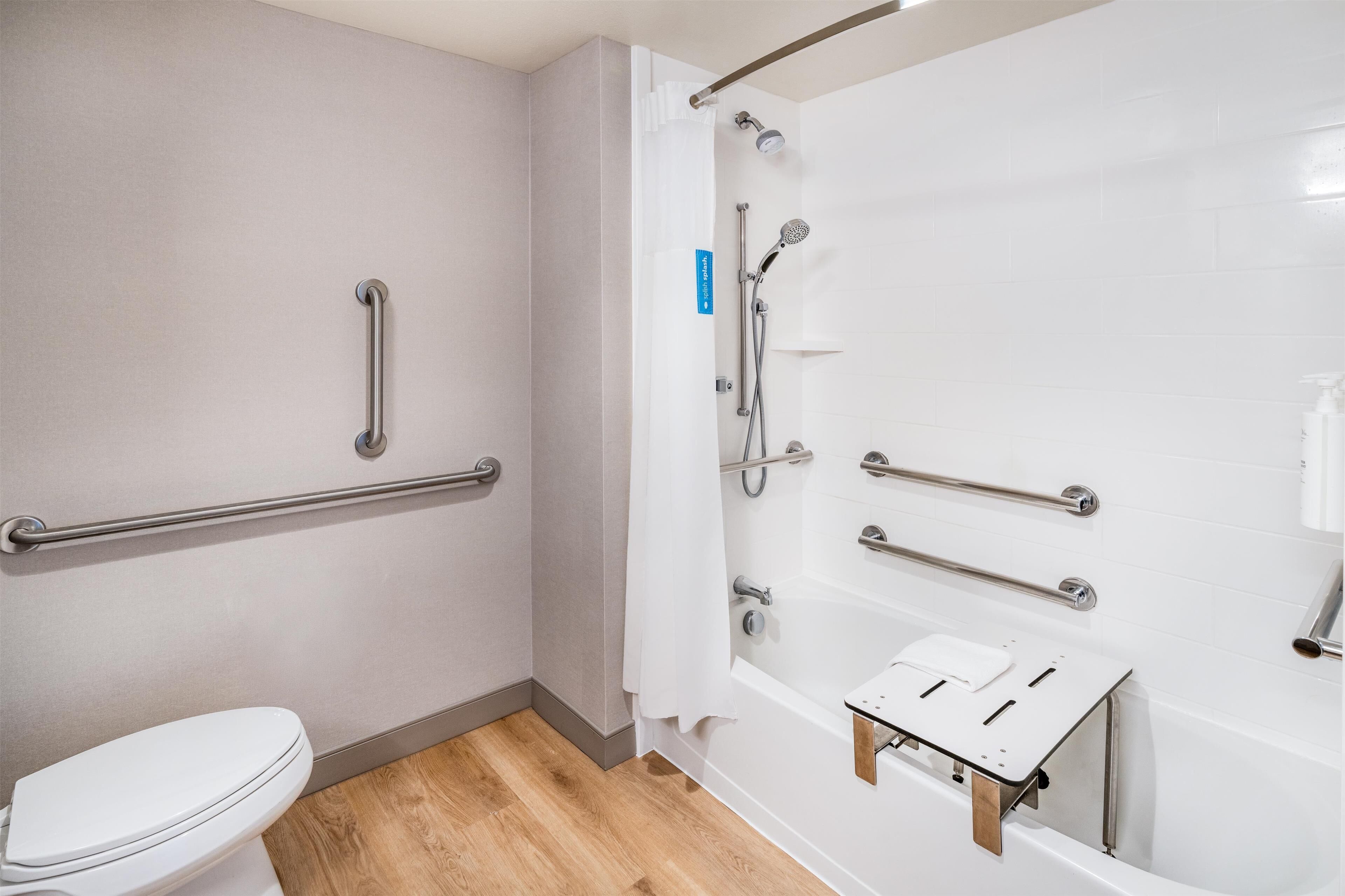 A bathroom with a white toilet, a shower with grab bars, and a bathtub with a side table.