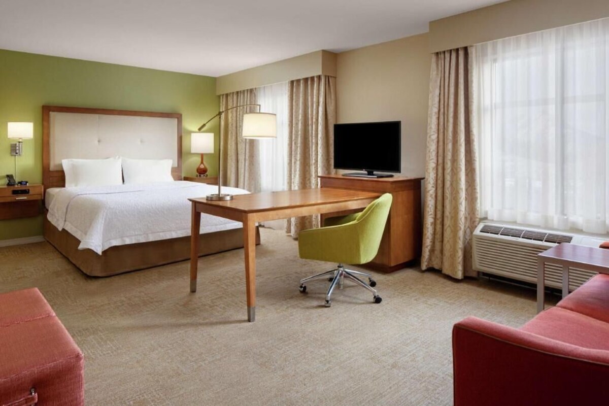A hotel room with a bed, desk, chair, TV, and a red couch.