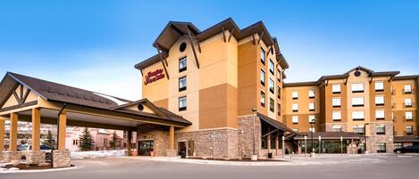 A multi-story hotel with a prominent 'Hampton Inn' sign, a covered entrance, and a parking lot.