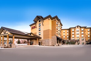 Um hotel com vários andares, um destaque com o letreiro 'Hampton Inn', uma entrada coberta e um estacionamento.