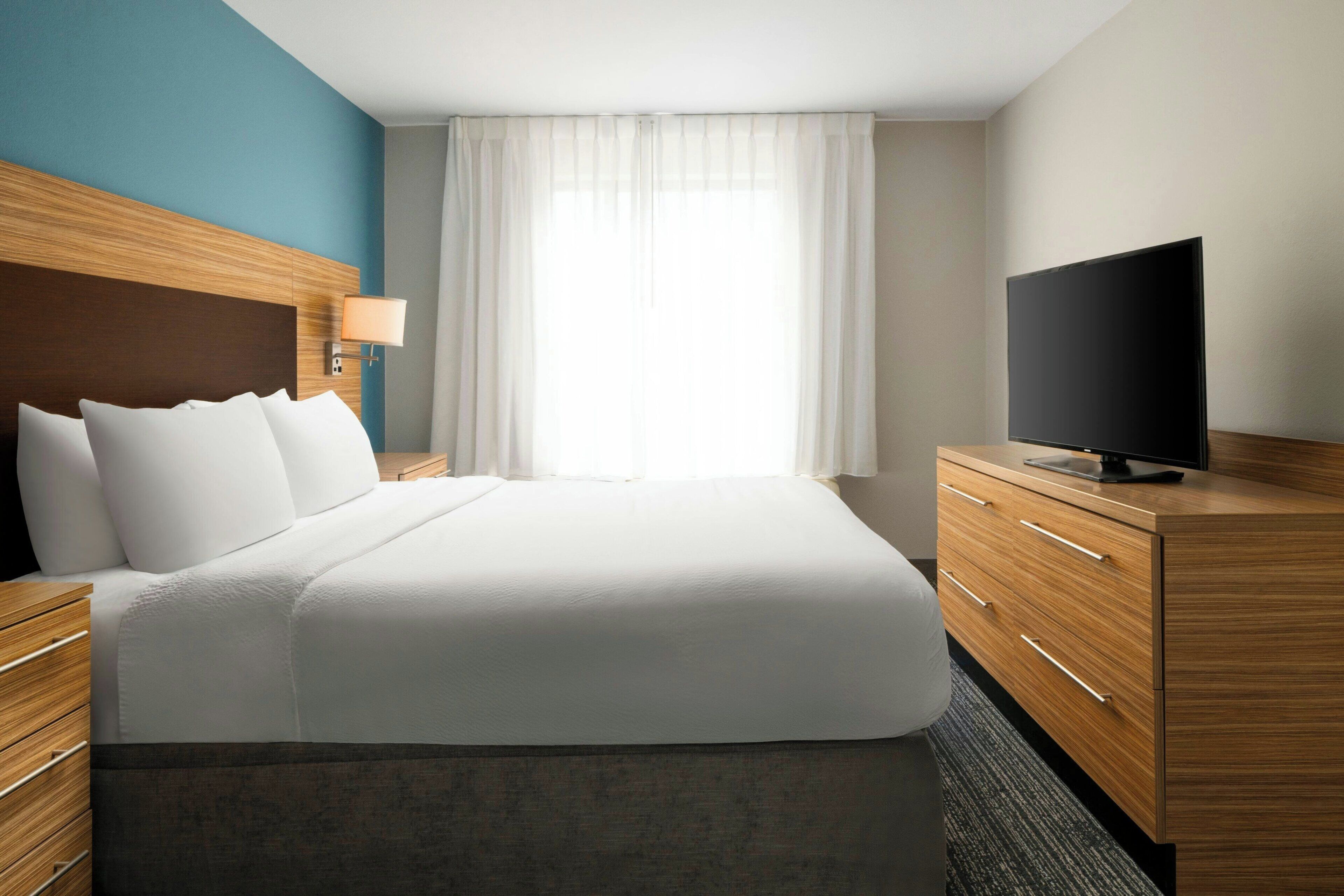 Camera d'albergo con un letto grande, una televisione, un comodino e una finestra con tende.