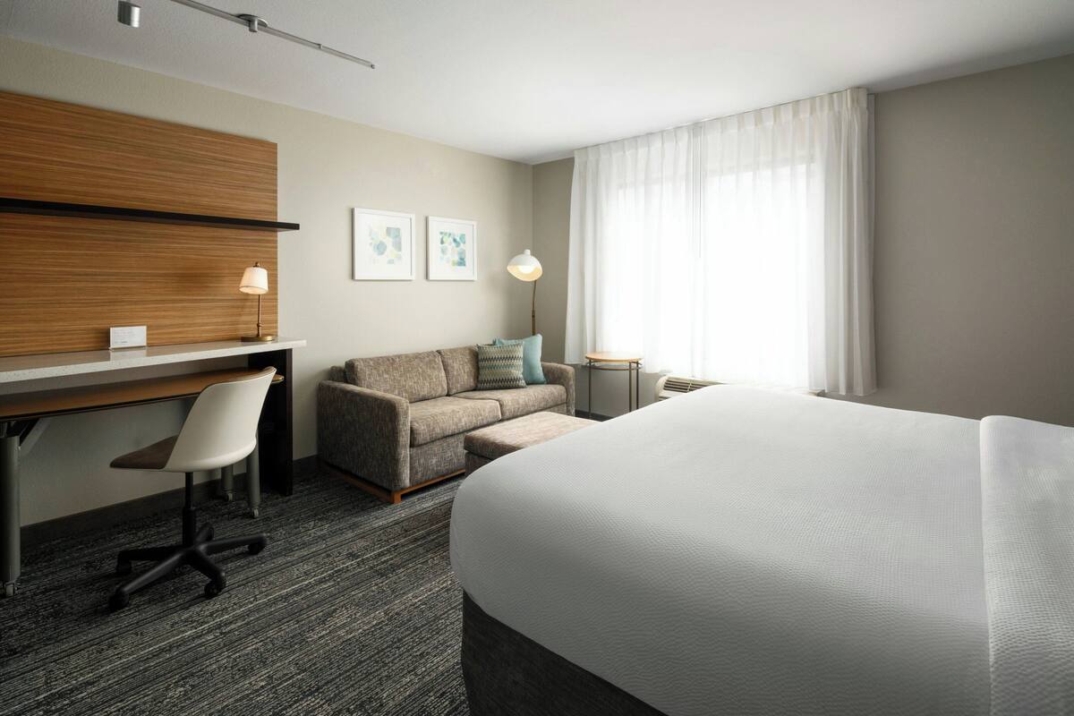 Habitación de hotel con cama, escritorio, silla, sofá, mesita y lámpara.