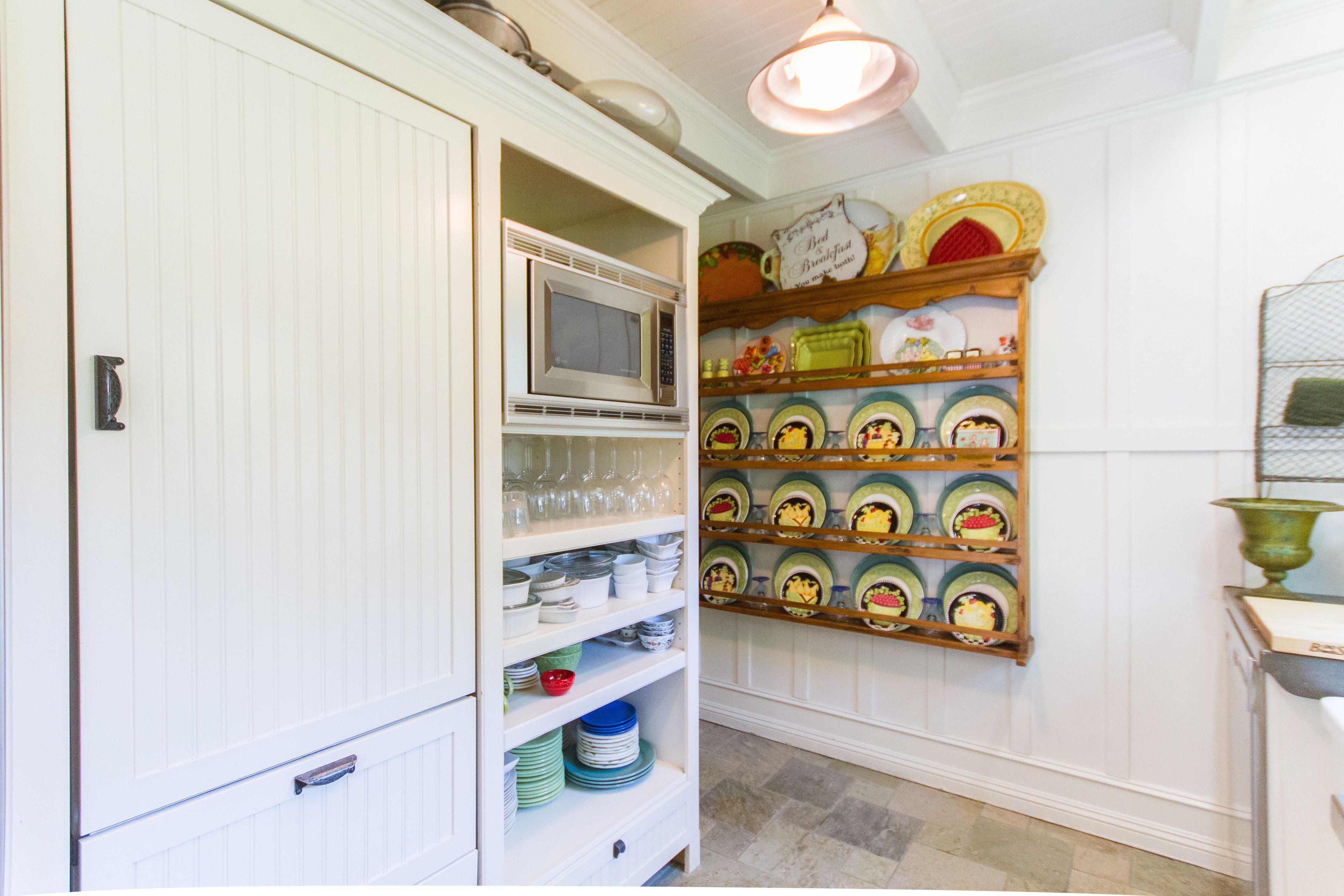 A kitchen with white cabinetry, a microwave, and shelves with colorful plates and bowls.