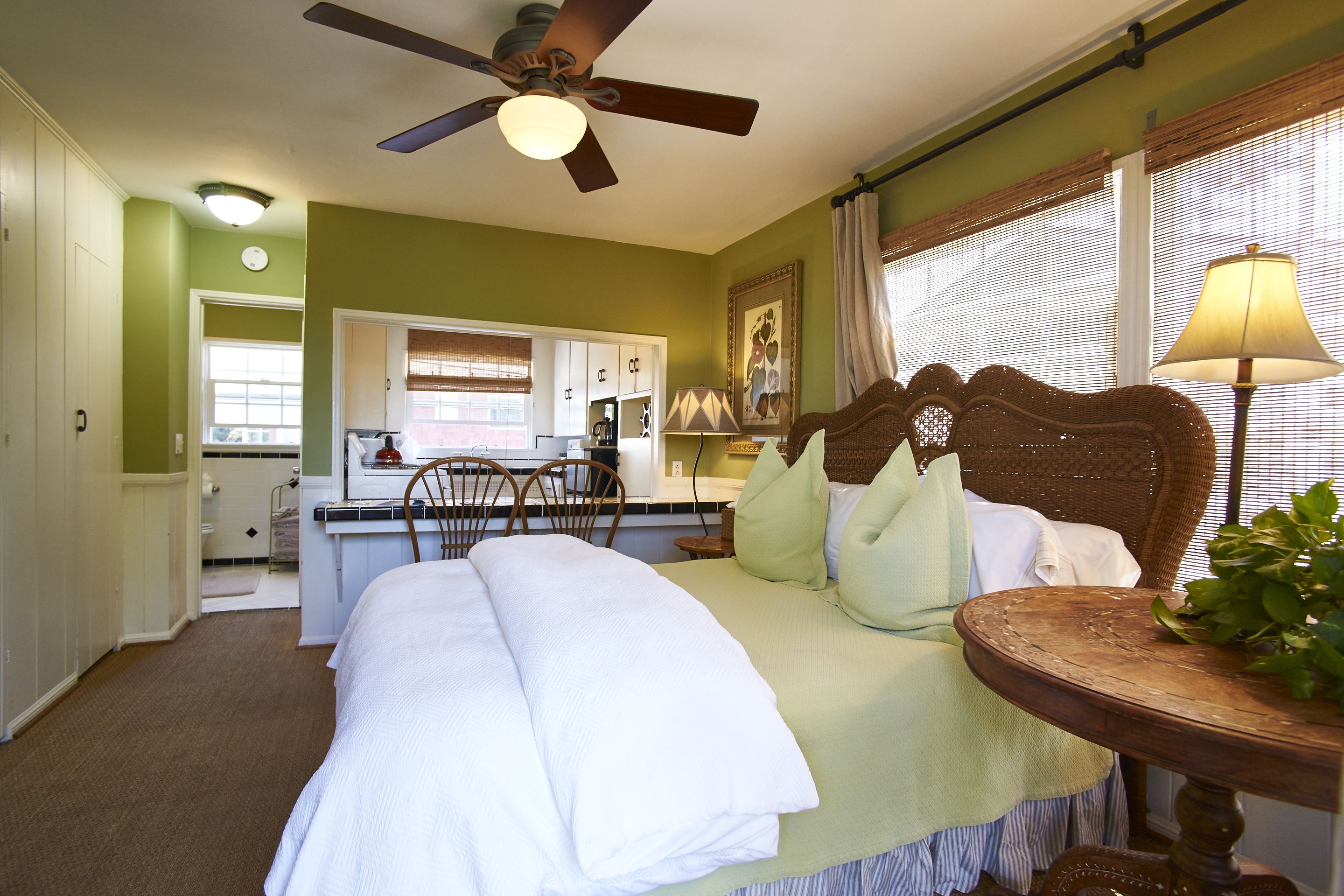 A bedroom with a bed, a ceiling fan, a dining area, and a window with blinds.