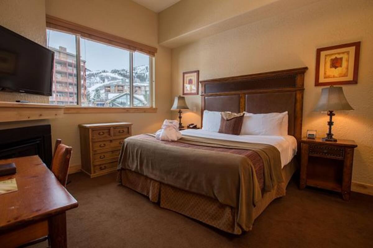 Habitación de hotel con cama, escritorio, televisión, ventana con vistas y dos lámparas de noche.