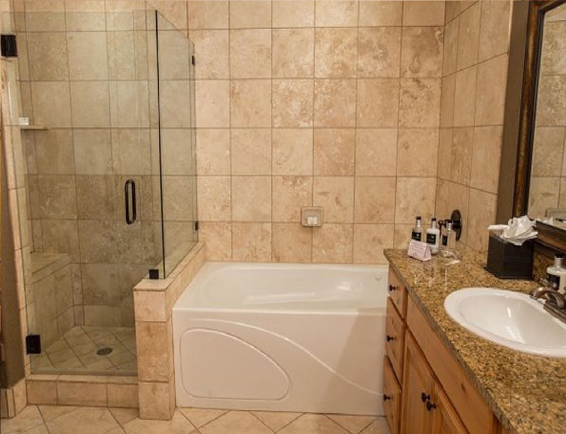 Un baño con ducha envuelta en cristal, una bañera blanca y un lavamanos con encimera de granito.