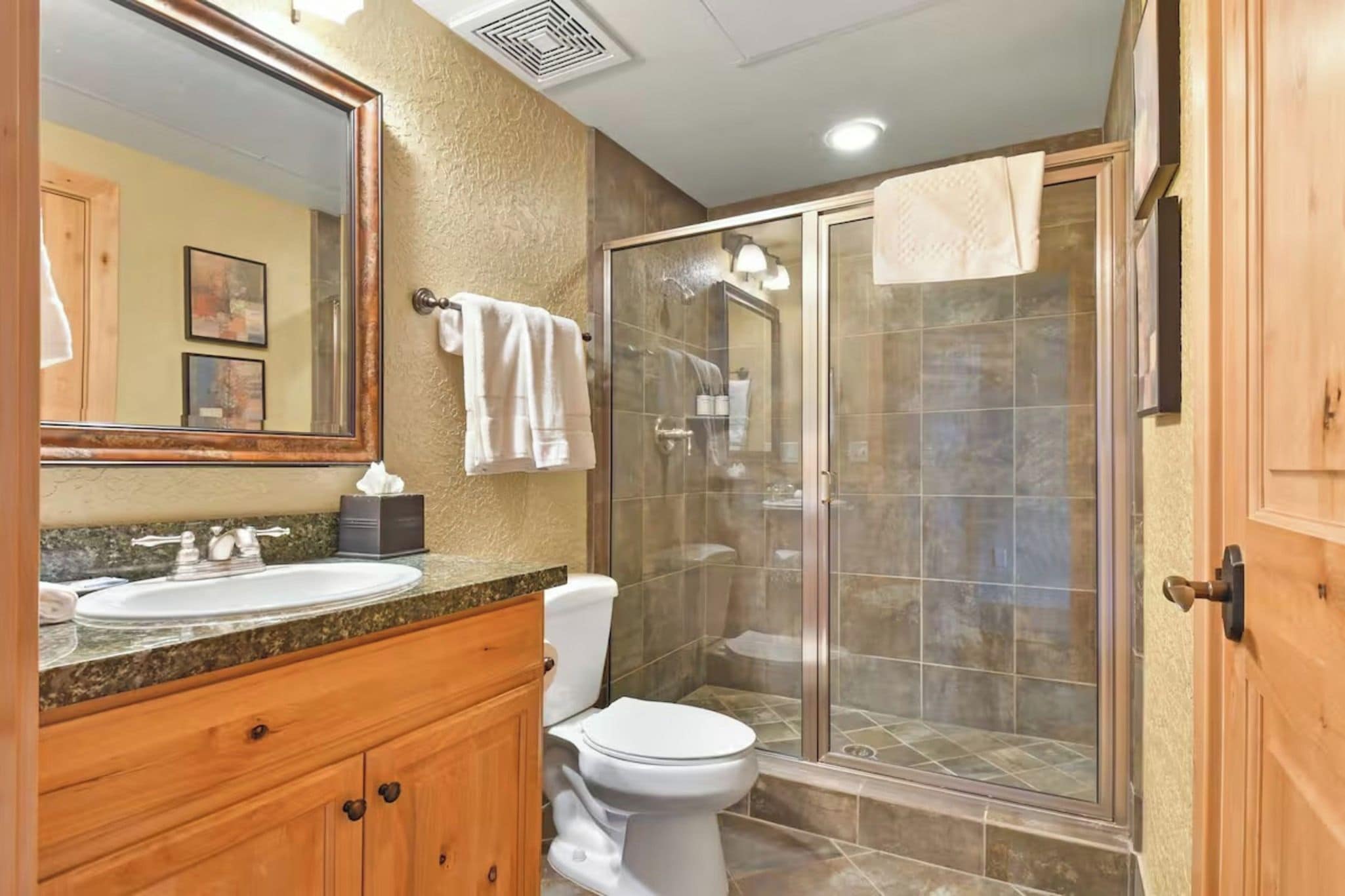 Une salle de bain avec un meuble-lavabo en bois, des toilettes blanches, une douche à parois de verre et un grand miroir.