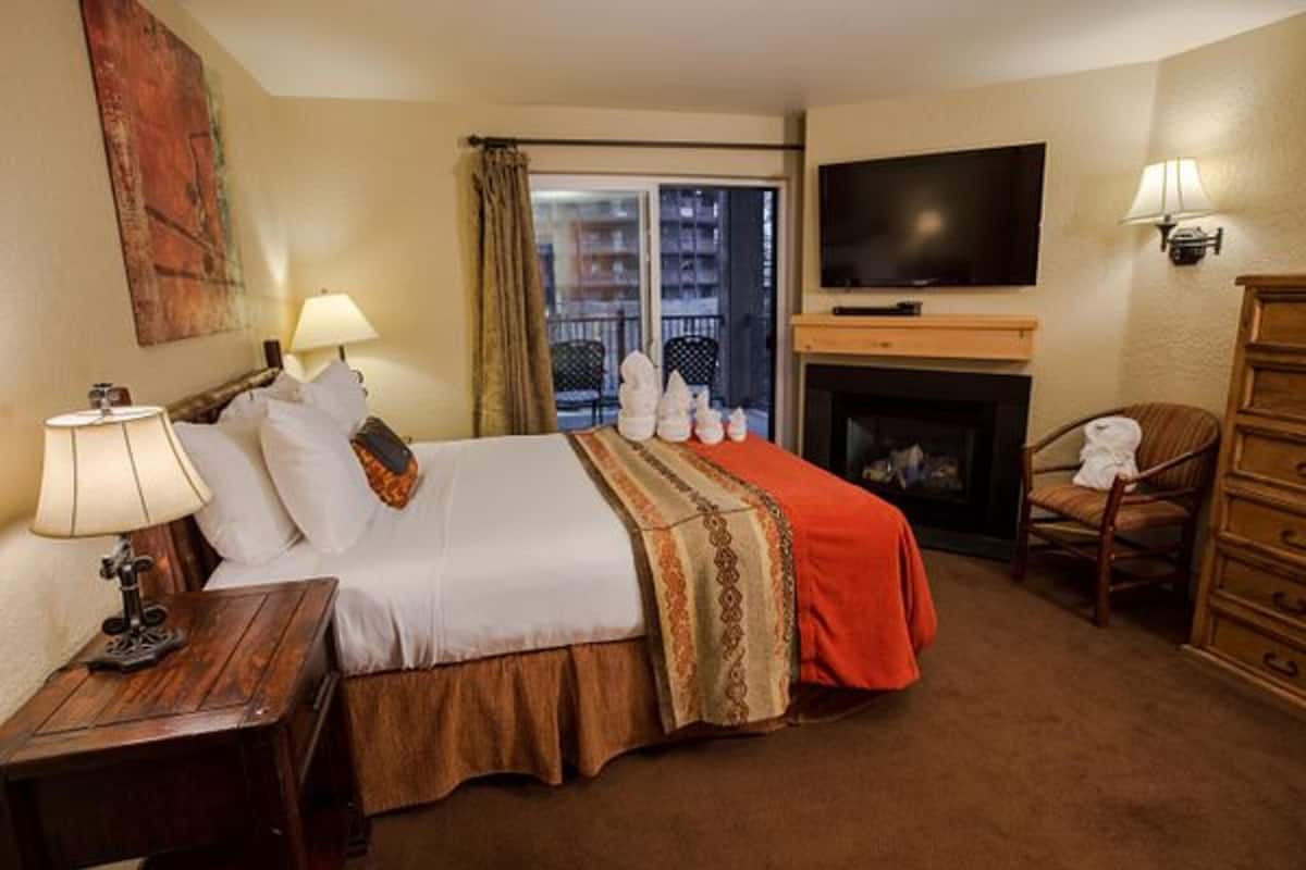 Ett hotellrum med en säng, en TV, en öppen spis, en stol och ett fönster med gardiner.