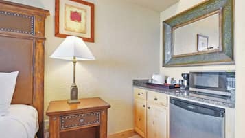 A hotel room with a bed, a bedside lamp, a small table with a lamp, a microwave, and a dishwasher.