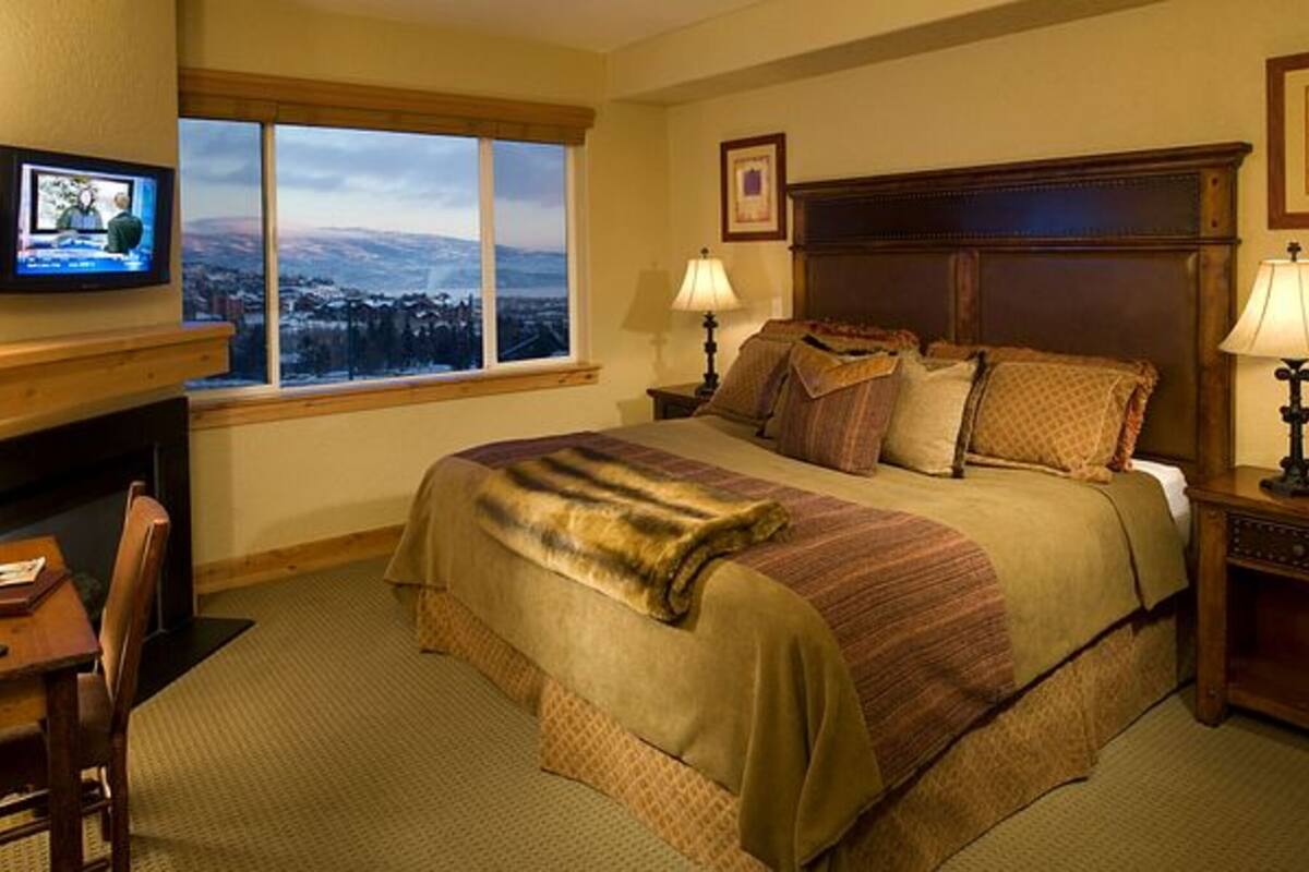 Habitación de hotel con una cama grande, un escritorio con silla, televisor y ventana con vista.