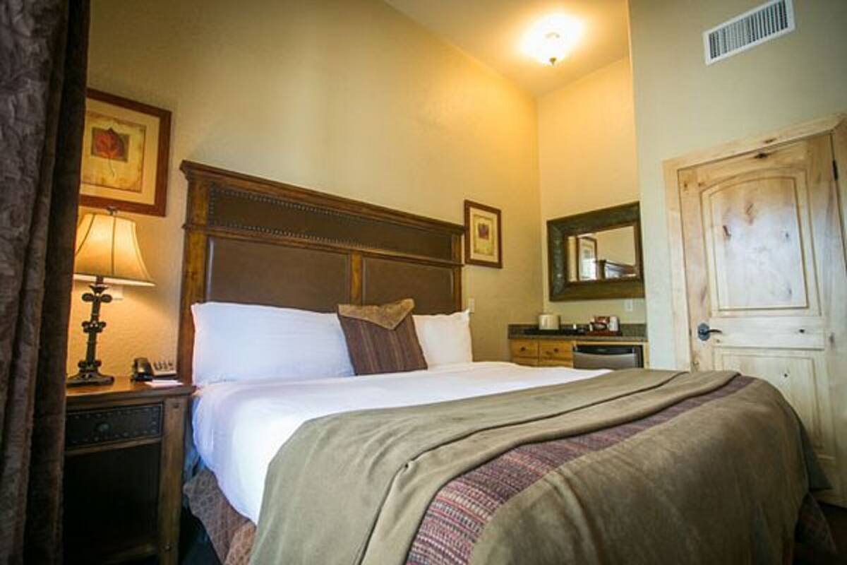 Una habitación de hotel con cama, mesita de noche, lámpara, cómoda, espejo y puerta.