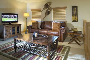 Una sala de estar con un sofá de cuero, una mesa de centro, un televisor y una estantería.