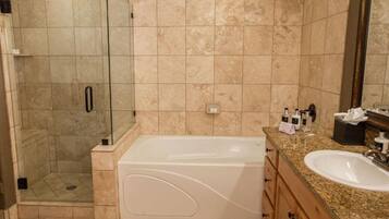 A bathroom with a glass-enclosed shower, a white bathtub, a granite countertop, and a sink.