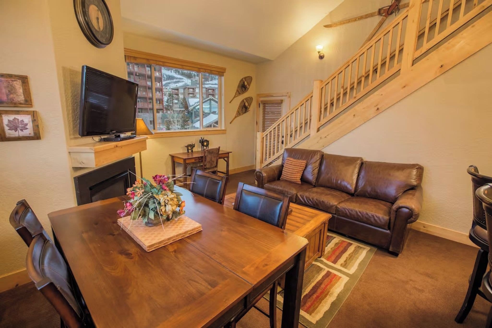 A cozy living room with a wooden dining table, leather sofa, and a staircase.