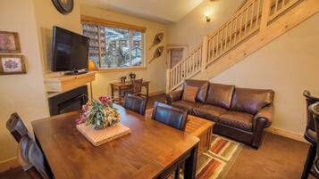 A cozy living room with a wooden dining table, leather sofa, and a staircase.