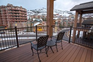 Varanda com duas cadeiras, um deck de madeira e vista para montanhas nevadas e edifícios.