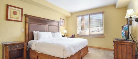 A hotel room with a large bed, bedside tables, a window with blinds, and a wall-mounted TV.